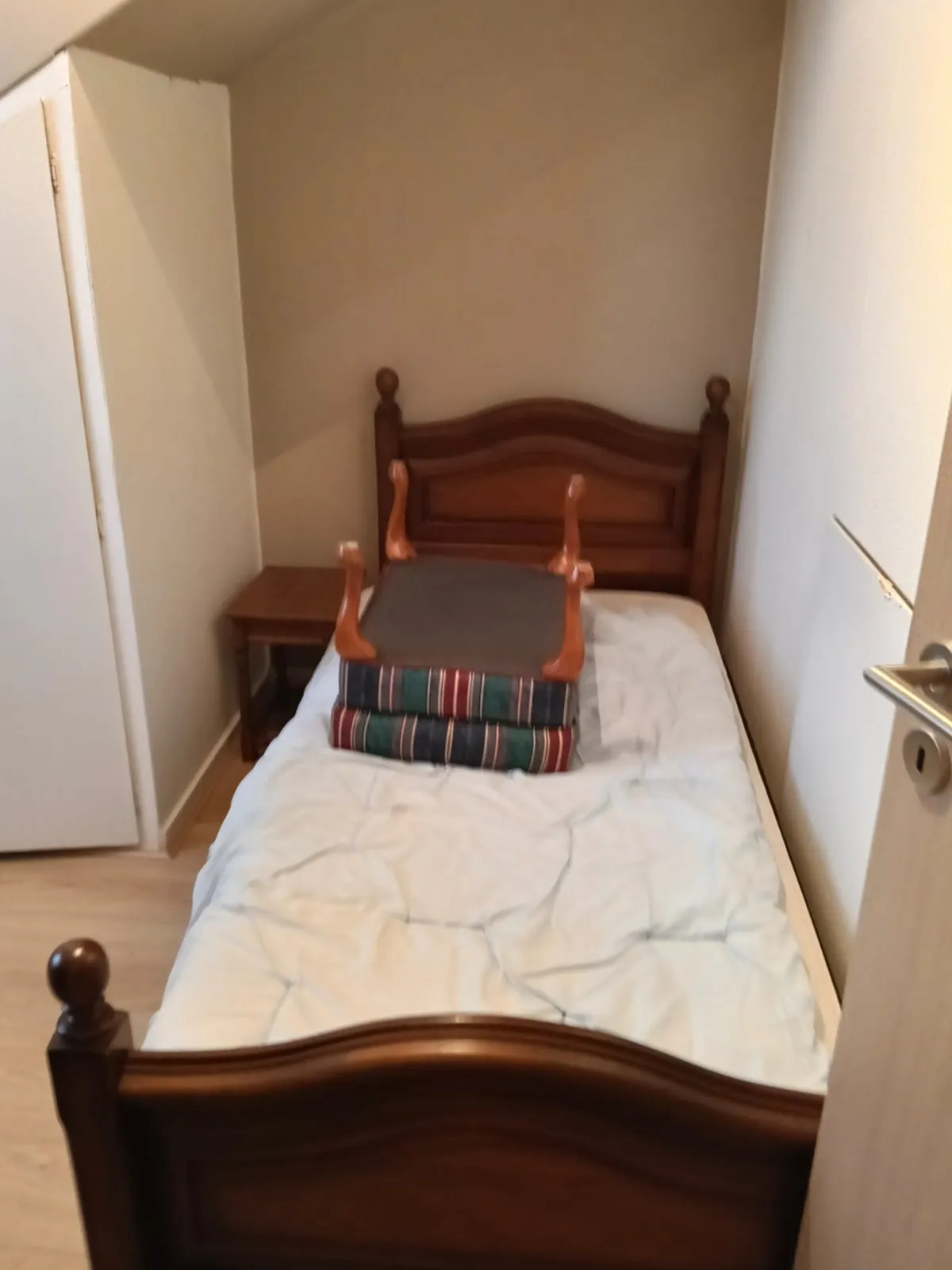 Houten eenpersoonsbed met matras in een kleine slaapkamer
