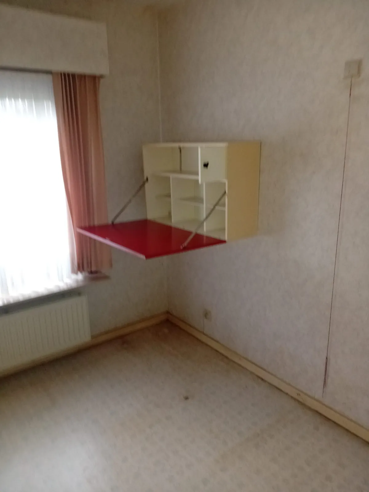 Kamer met een rood klapbureau aan de muur en een radiator onder het raam