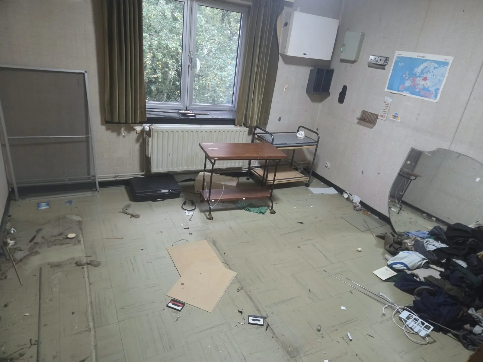 Kamer met losse spullen, kleding en afval op de vloer